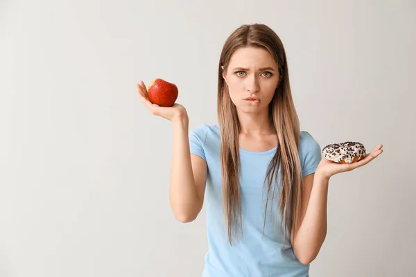 Stressed woman choosing between healthy and unhealthy food on light background. Diet concept — Stock Photo, Image