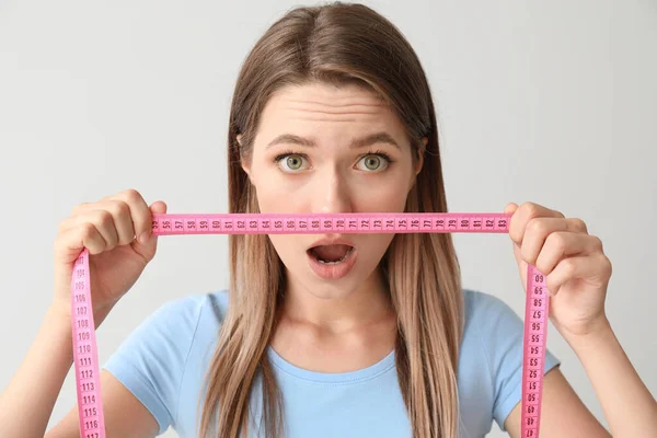 Shocked woman with measuring tape on light background. Diet concept — Stock Photo, Image