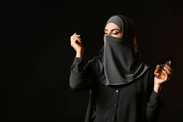 Schöne muslimische Frau mit Parfüm auf dunklem Hintergrund — Stockfoto