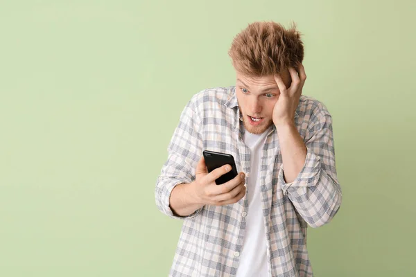 Шокированный молодой человек с мобильным телефоном на цветном фоне — стоковое фото