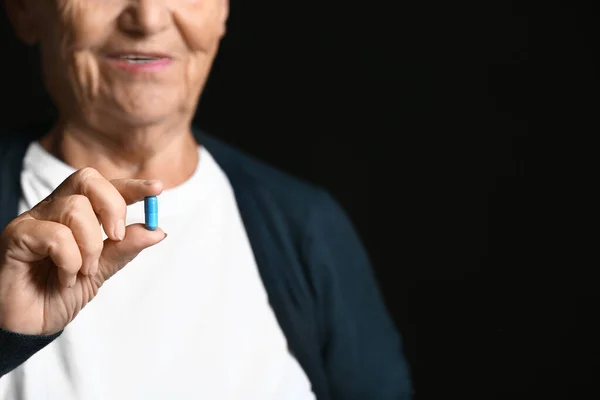 Mujer anciana con píldora sobre fondo oscuro —  Fotos de Stock