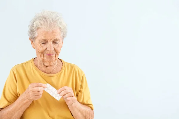 Elderly woman with pills on light background — Stock Photo, Image