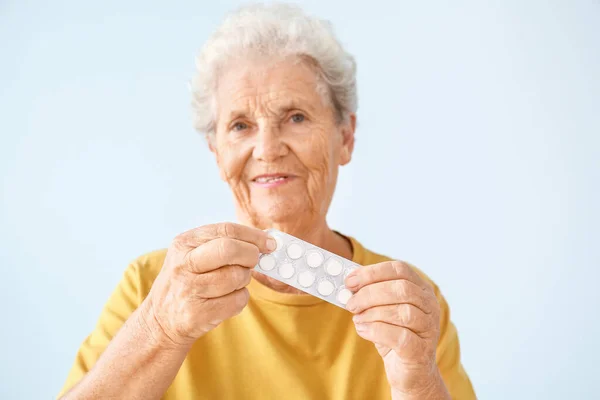 Elderly woman with pills on light background — Stock Photo, Image