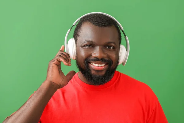 Handsome African-American man listening to music on color background — Stock Photo, Image