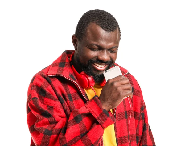 Handsome African-American man singing and using mobile phone as microphone on white background — Stock Photo, Image