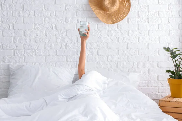 Mladá žena se sklenicí vody ležící v posteli — Stock fotografie