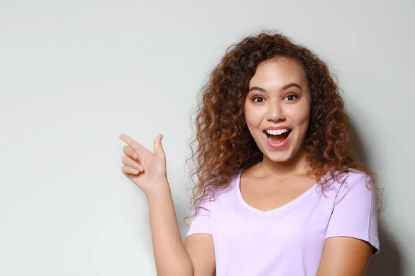Portrait of excited African-American woman pointing at something on light background — Stock Photo, Image