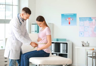 Jinekolog klinikte kadının karnının ölçüsünü alıyor.