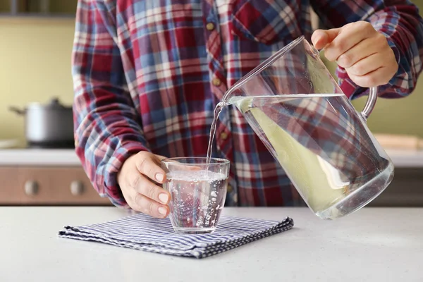Mujer vertiendo agua dulce de la jarra en un vaso sobre la mesa — Foto de Stock