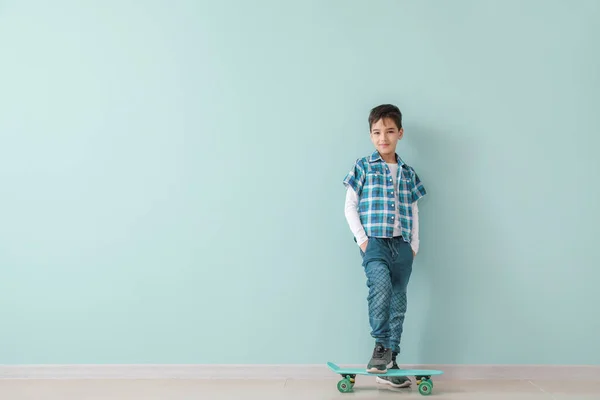 색 벽에 스케이트보드를 달고 있는 귀엽고 유행하는 소년 — 스톡 사진