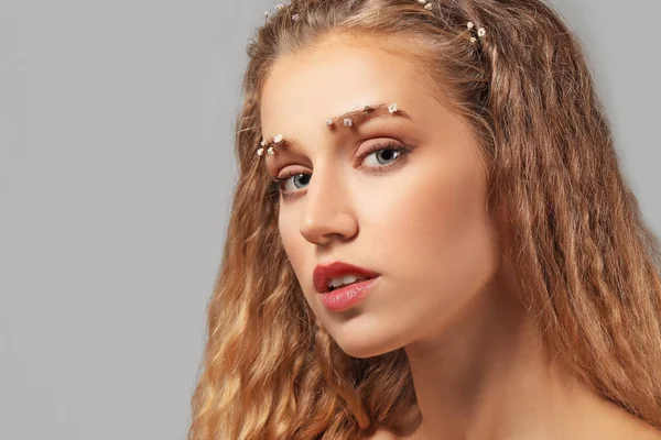 Mujer joven con cejas creativas sobre fondo gris — Foto de Stock