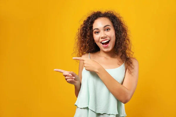 Portret van Happy African-Amerikaanse vrouw wijzend op iets op kleur achtergrond — Stockfoto