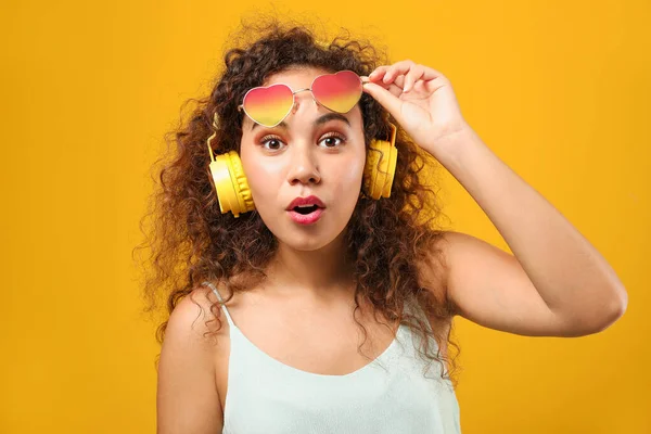 Portrait of surprised African-American woman with headphones on color background — Stock Photo, Image