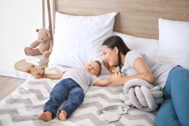 Asyalı anne ve sevimli küçük bebek yatakta oynuyor