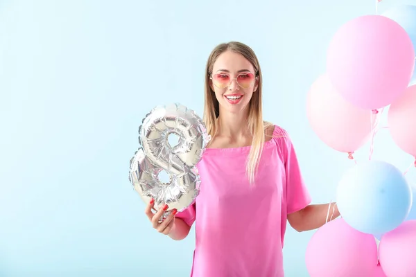 Beautiful young woman with figure 8 and air balloons on color background. International Women's Day celebration — Stock Photo, Image