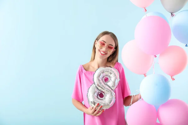 Bella giovane donna con figura 8 e palloncini d'aria su sfondo di colore. Festa internazionale della donna — Foto Stock