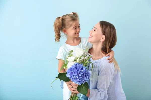 Little girl and her mother with flowers on color background — Stock Photo, Image