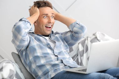 Evde dizüstü bilgisayarı olan şaşırmış genç bir adam.