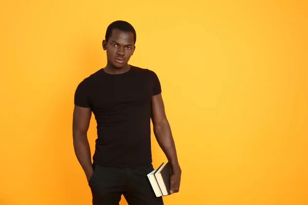 Handsome African-American man with books on color background