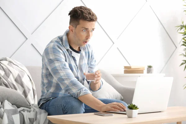 Shocked young man with laptop at home — Stock Photo, Image