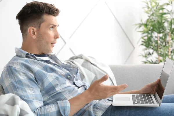 Shocked young man with laptop at home — Stock Photo, Image