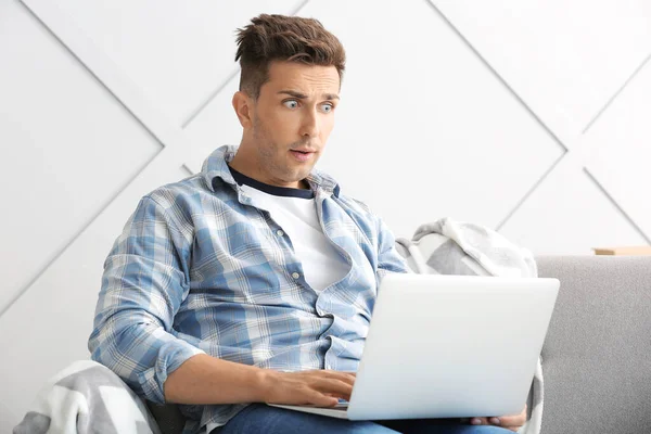 Shocked young man with laptop at home — Stock Photo, Image