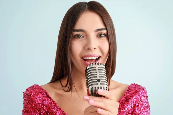 Hermosa joven cantante femenina con micrófono sobre fondo claro —  Fotos de Stock