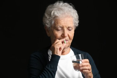 Yaşlı bir kadın karanlık arka planda ilaç alıyor.