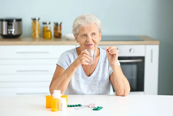 Elderly woman taking medicine at home