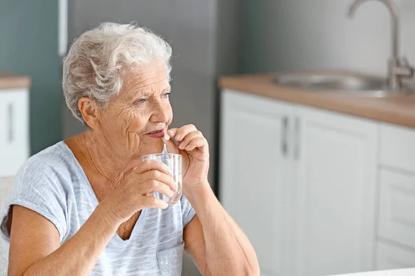 Elderly woman taking medicine at home — Stock Photo, Image