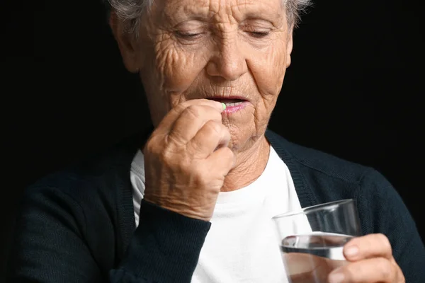 Mujer mayor tomando medicamentos sobre fondo oscuro —  Fotos de Stock