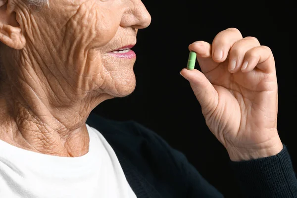 Elderly woman taking medicine on dark background, closeup — Stock Photo, Image
