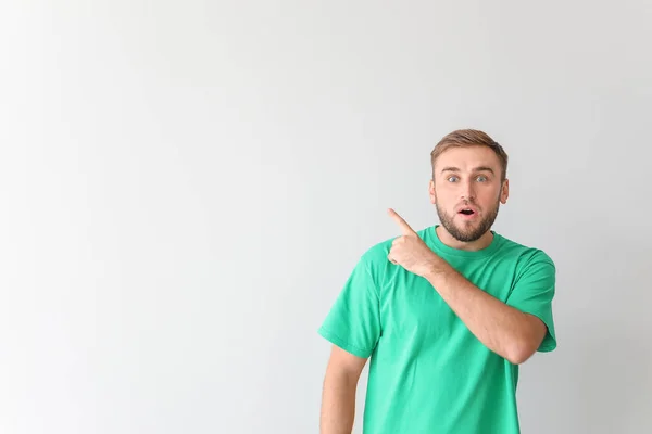 Surprised young man pointing at something on light background — Stock Photo, Image