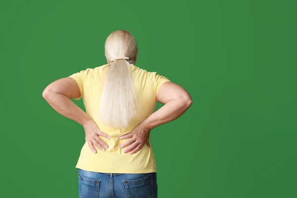 Зріла жінка страждає від болю в спині на кольоровому фоні — стокове фото