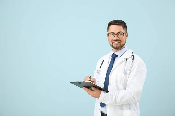 Portrét mužského lékaře se schránkou na barevném pozadí — Stock fotografie