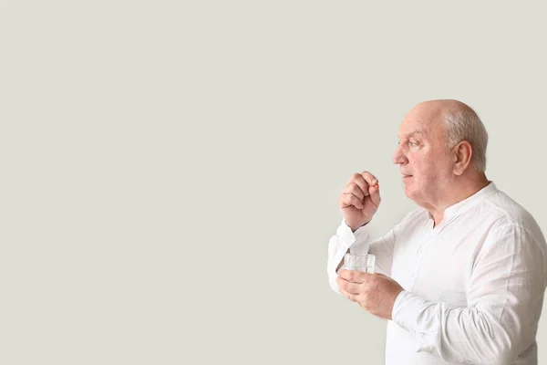 Elderly man taking medicine on light background — Stock Photo, Image