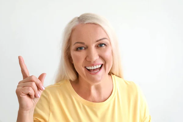 Portrait of beautiful mature woman with raised index finger on light background — Stock Photo, Image