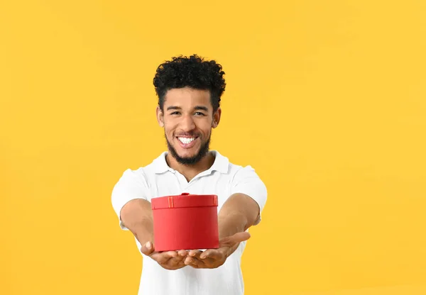 Portrait d'homme afro-américain heureux avec un cadeau sur fond de couleur — Photo