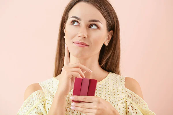 Bedachtzame jonge vrouw met lippenstift op kleur achtergrond — Stockfoto