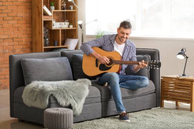 Yakışıklı adam evde gitar çalıyor.