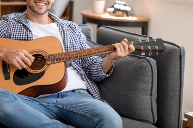 Yakışıklı adam evde gitar çalıyor.