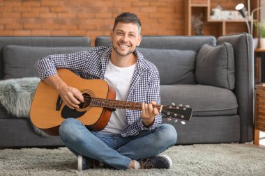 Yakışıklı adam evde gitar çalıyor.
