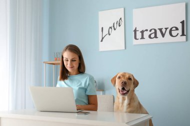 Evde dizüstü bilgisayar kullanan sevimli köpekli güzel genç bir kadın.