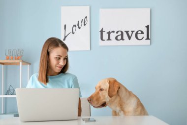 Evde dizüstü bilgisayar kullanan sevimli köpekli güzel genç bir kadın.