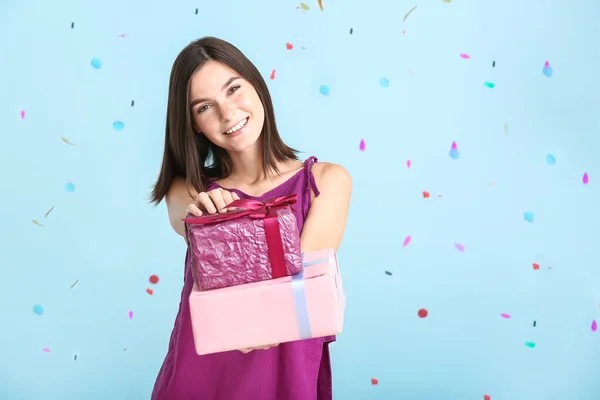 Beautiful young woman with gifts and falling confetti on color background — Stock Photo, Image