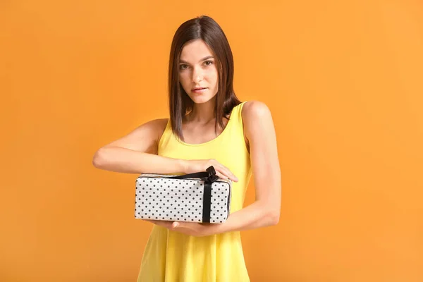 Schöne junge Frau mit Geschenk auf farbigem Hintergrund — Stockfoto