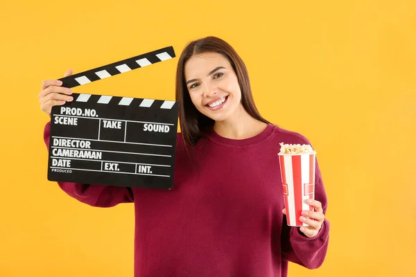 Młoda kobieta z popcornem i klapką filmową na kolorowym tle — Zdjęcie stockowe