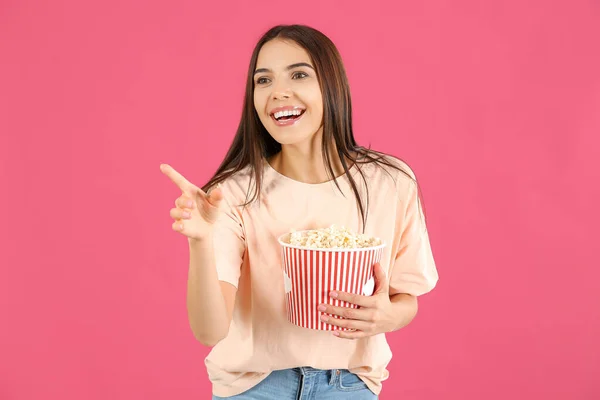 Young woman with popcorn pointing at something on color background — Stock Photo, Image