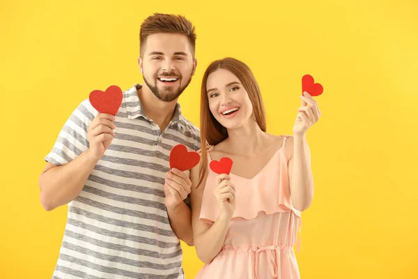 Retrato de feliz pareja joven con corazones de papel sobre fondo de color —  Fotos de Stock