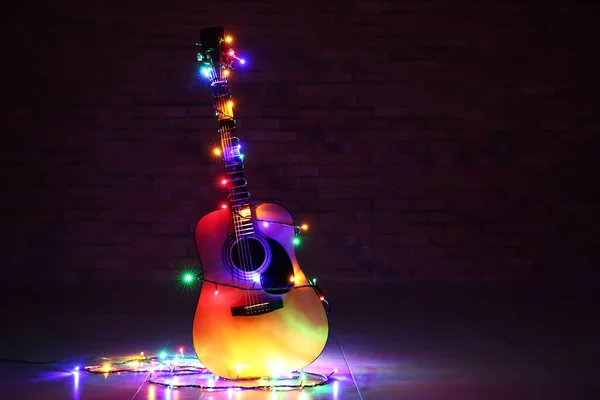 Akoestische gitaar met kerstverlichting tegen donkere achtergrond — Stockfoto